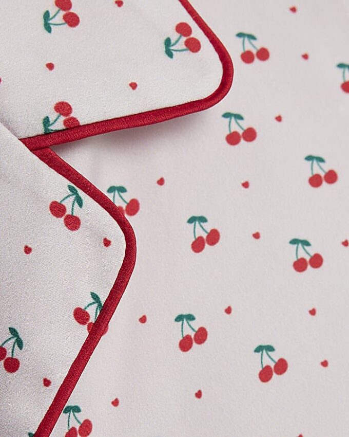 Flickpyjamas i krämfärgat satin med körsbärsmönster Flickpyjamas i krämfärgat satin med körsbärsmönster
